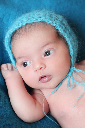 Fotografin Baby Düsseldorf: Baby mit wachen blauen Augen und blauer Wollmütze auf blauer Wolldecke.