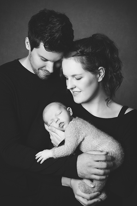 Babyfoto mit Eltern: Junges verliebtes Paar hält glücklich das Baby in den Armen und sieht es verliebt an.